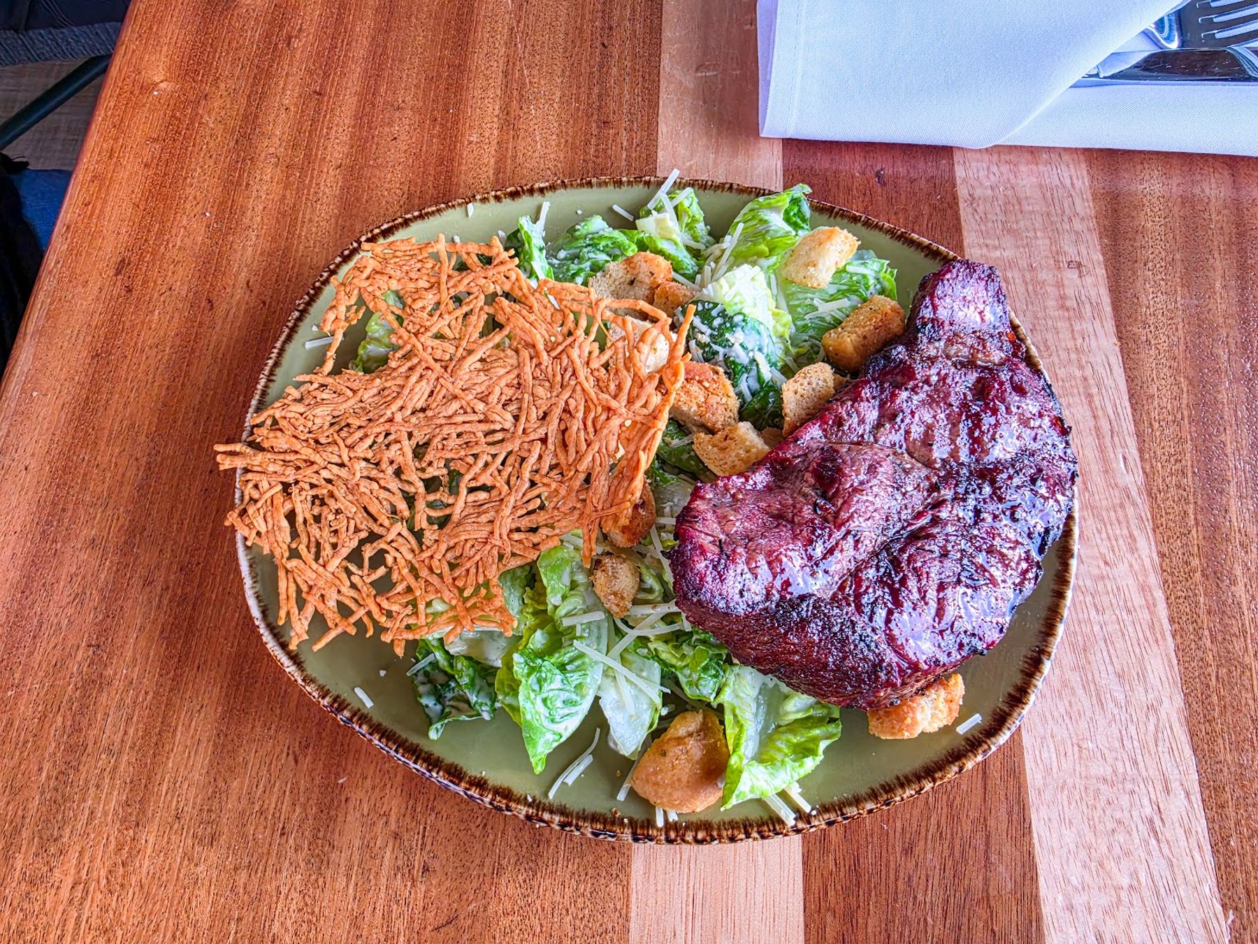 A composed salad and seared protein dish served on a wood table at Huggo's.