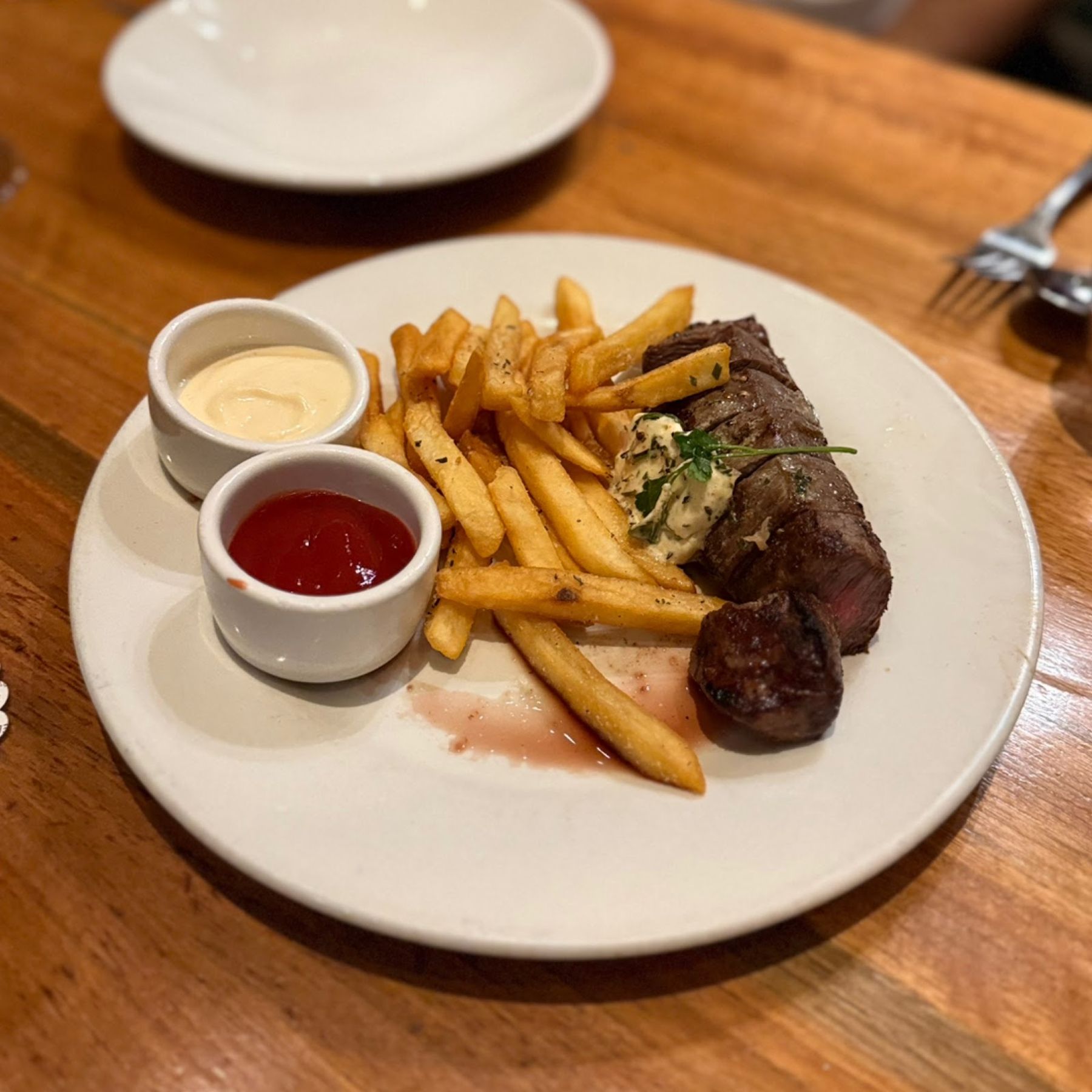 A steak and fries plate with sauces on a wood table at Merriman's Honolulu.