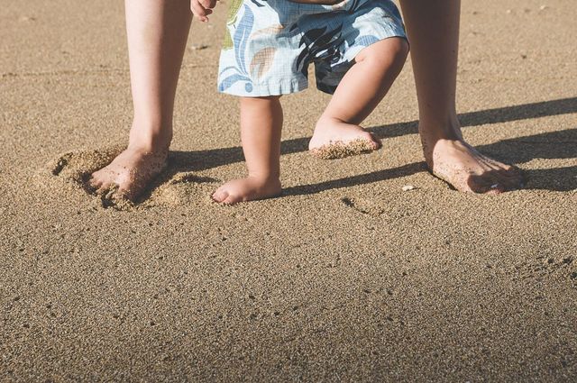 a toddler and his parent make footprints in the wet sand