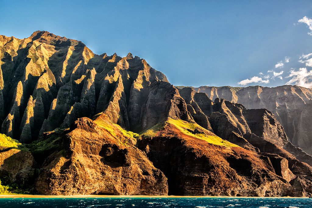 Sunlit Nā Pali Coast cliffs rising steeply above turquoise ocean under a clear blue sky