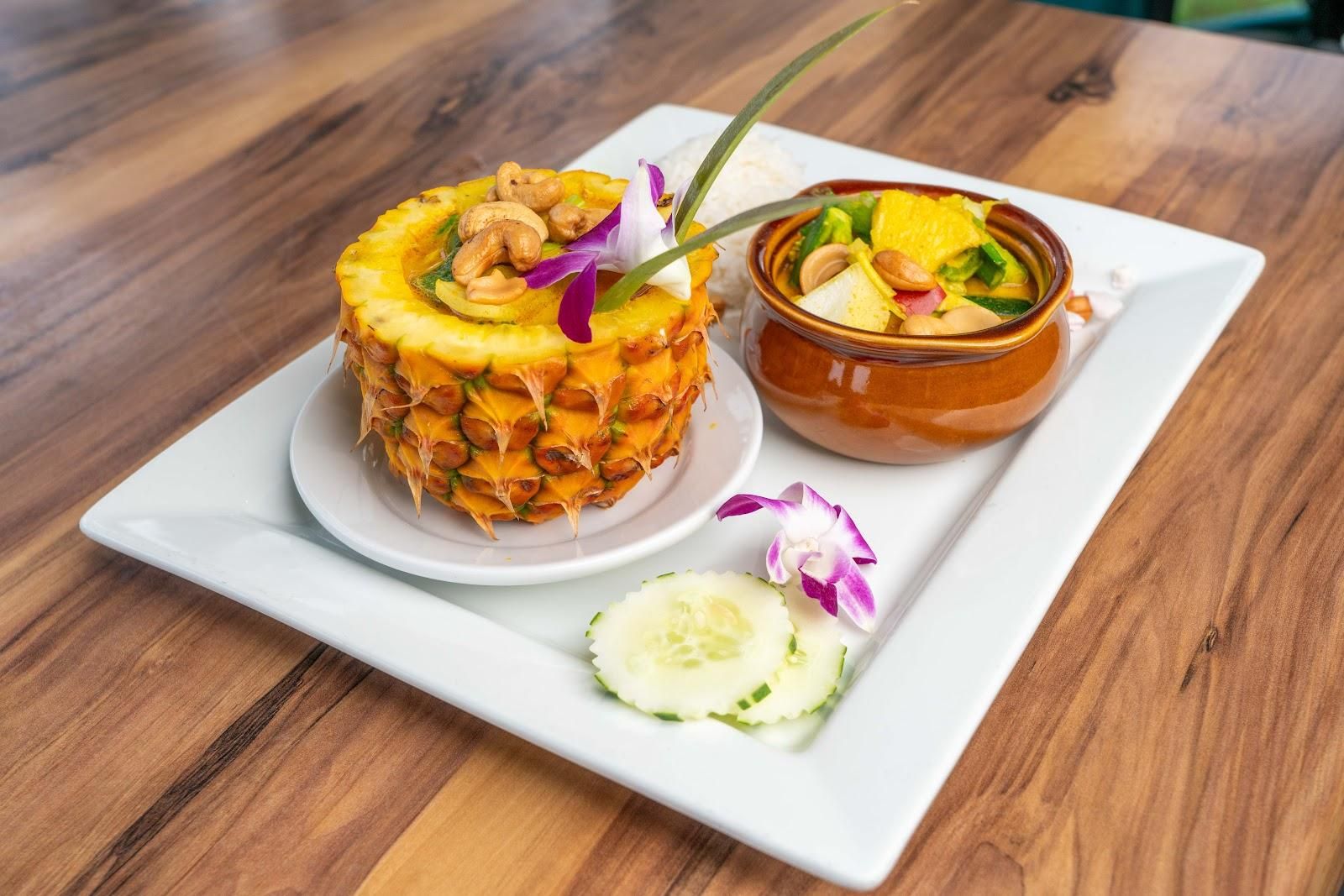 Thai-style pineapple–cashew curry in a pineapple shell with rice and cucumber slices, finished with edible orchids.