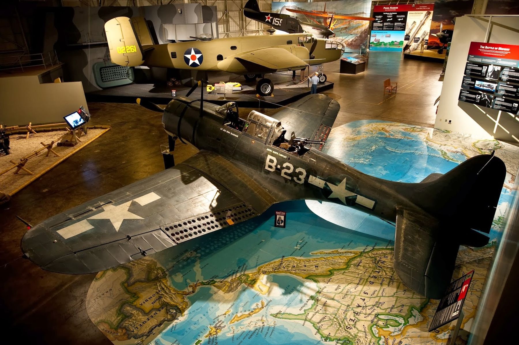 World War II aircraft displayed inside Pearl Harbor Aviation Museum above a floor map of the Pacific theater.