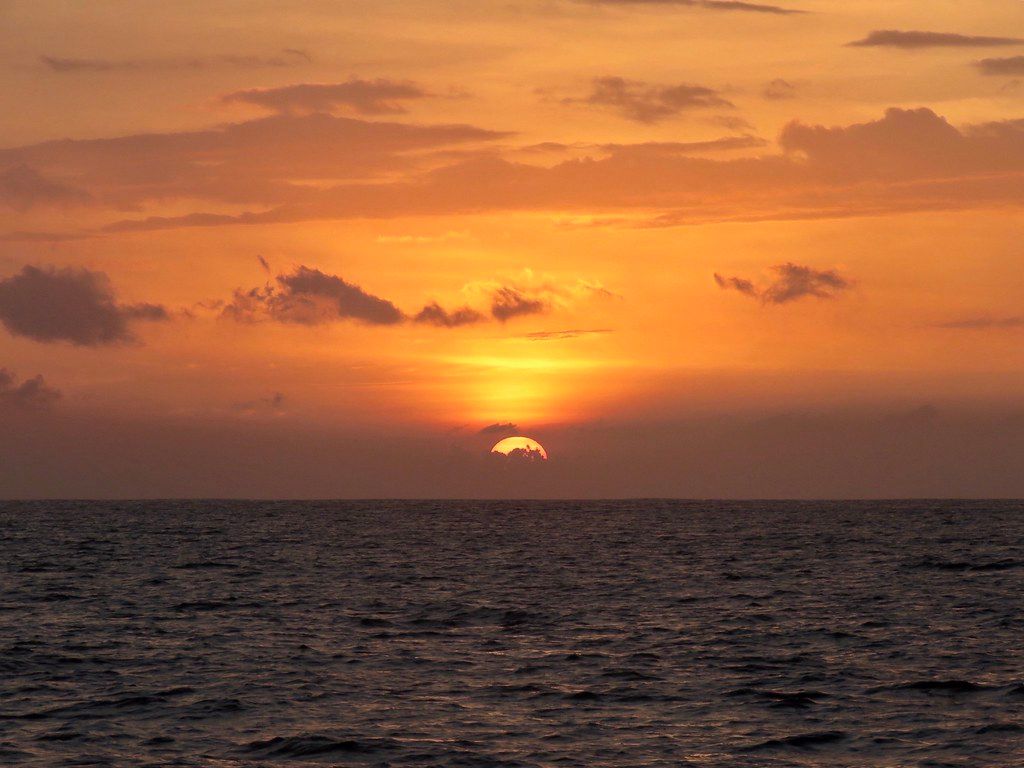 Orange sunset over the Pacific with the sun half-set on the horizon and dark rippled water in the foreground