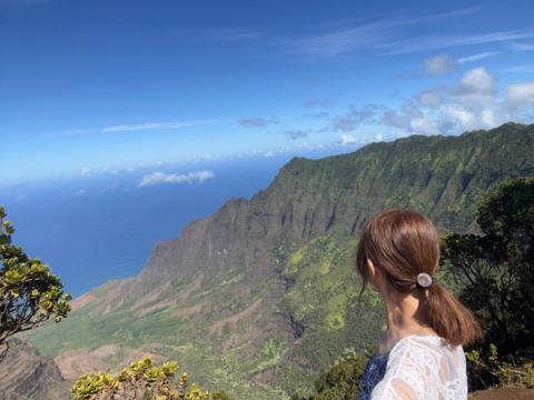 Hiker taking in the breathtaking view of Kalalau Valley from the lookout, with dramatic green cliffs dropping to the ocean