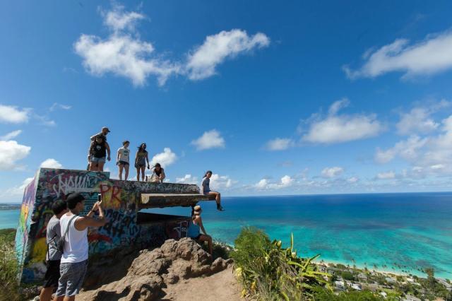 Hikers at the Lanikai Pillbox overlook above bright blue ocean water.
