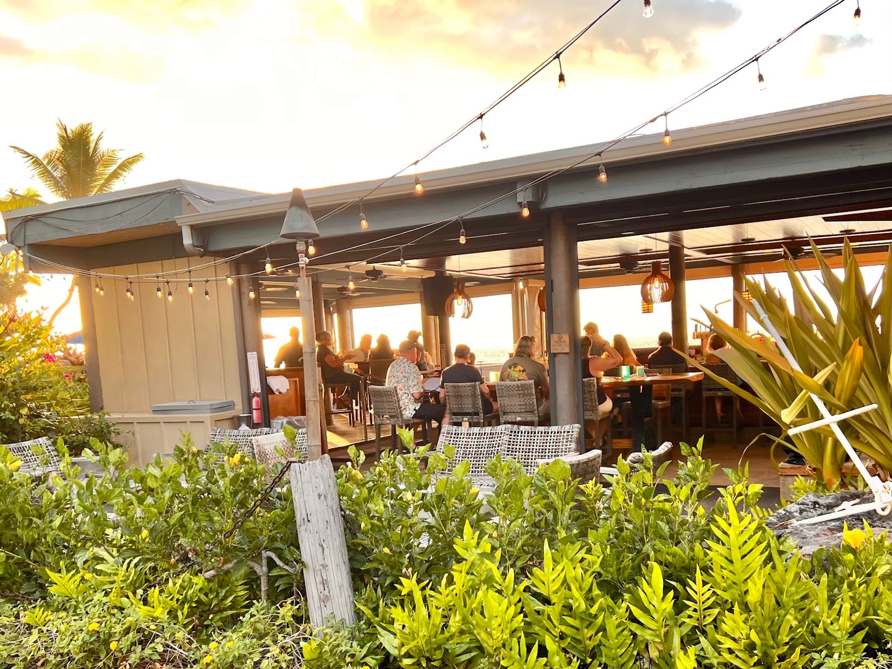 Open-air tables at Huggo's facing the Kona waterfront at golden hour.