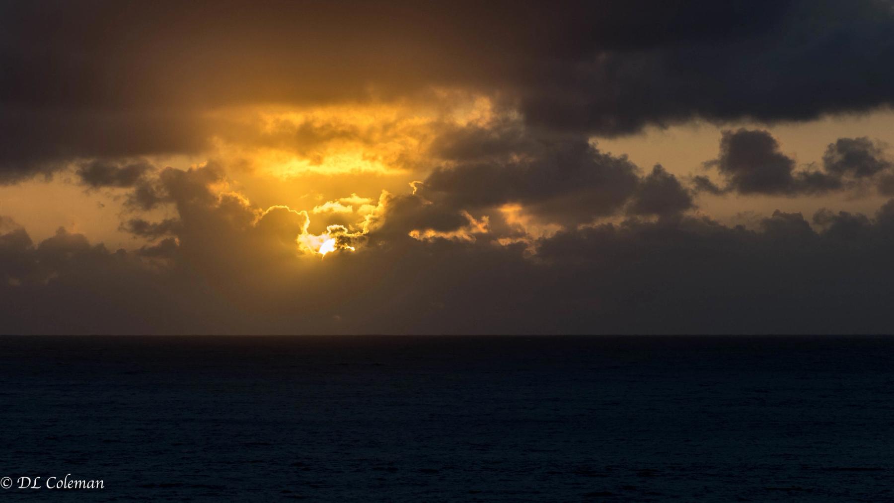Golden sunrise breaking through dark storm clouds above a calm ocean horizon