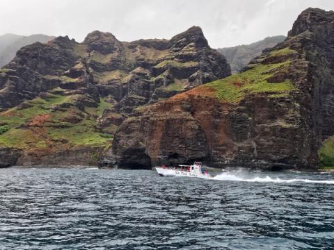 Tour catamaran cruising past the dramatic sea cliffs and sea caves of the Na Pali Coast