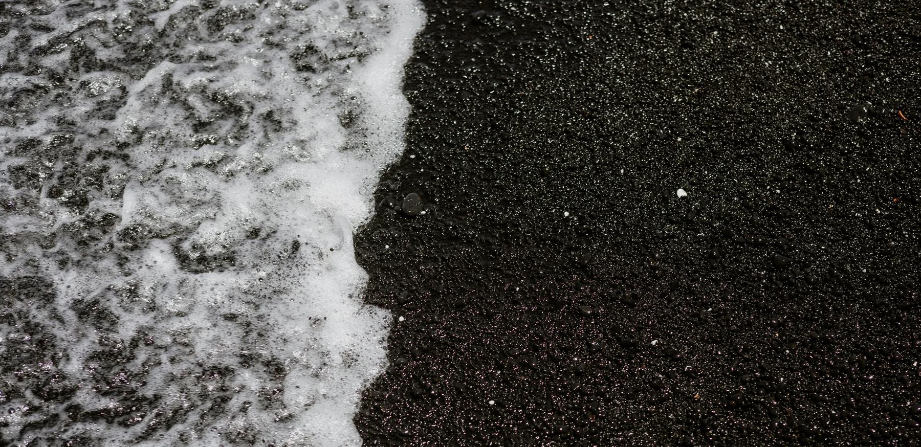 foamy surf laps the black sand of the beach