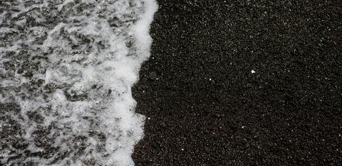foamy surf laps the black sand of the beach