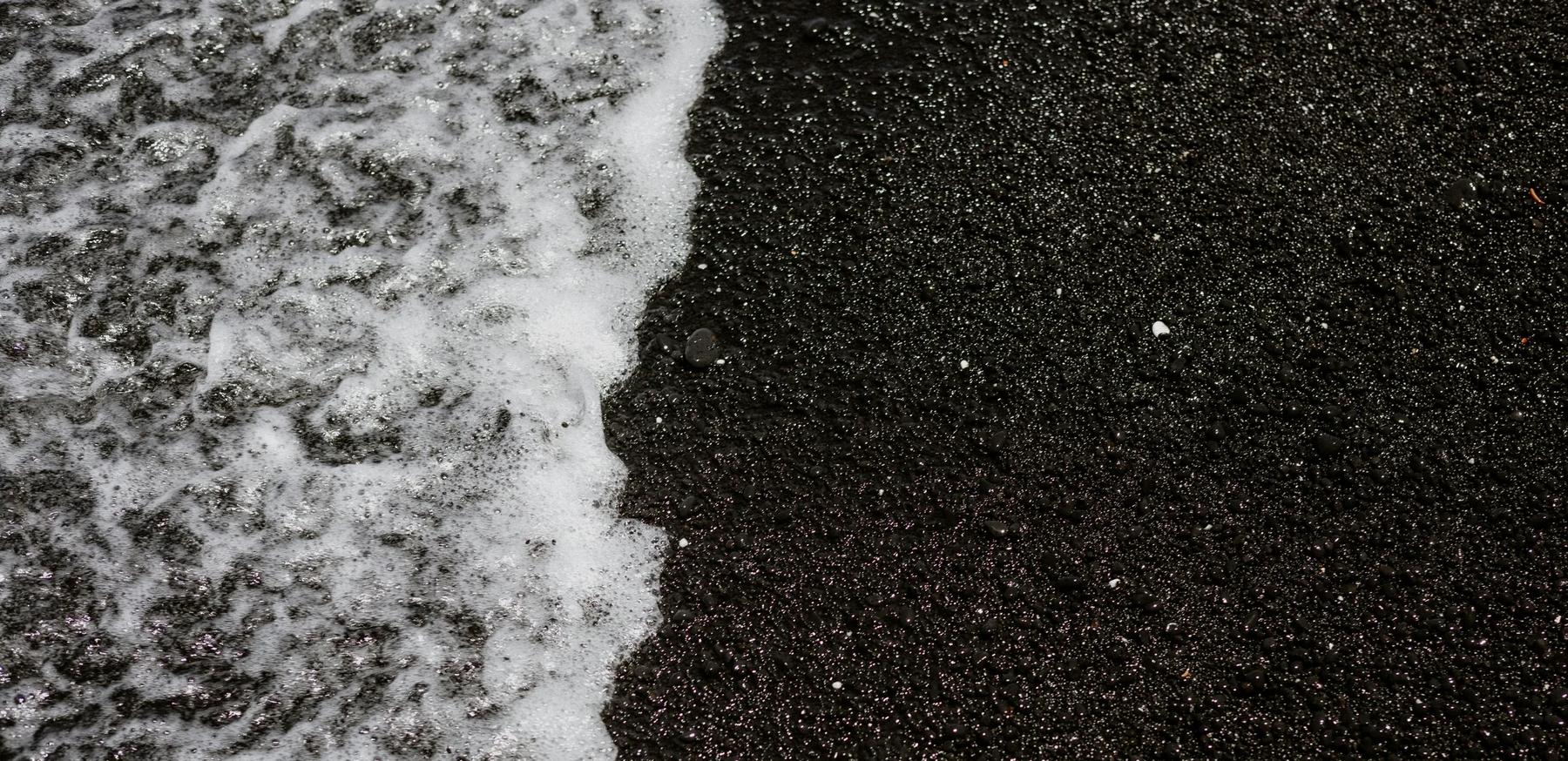 foamy surf laps the black sand of the beach