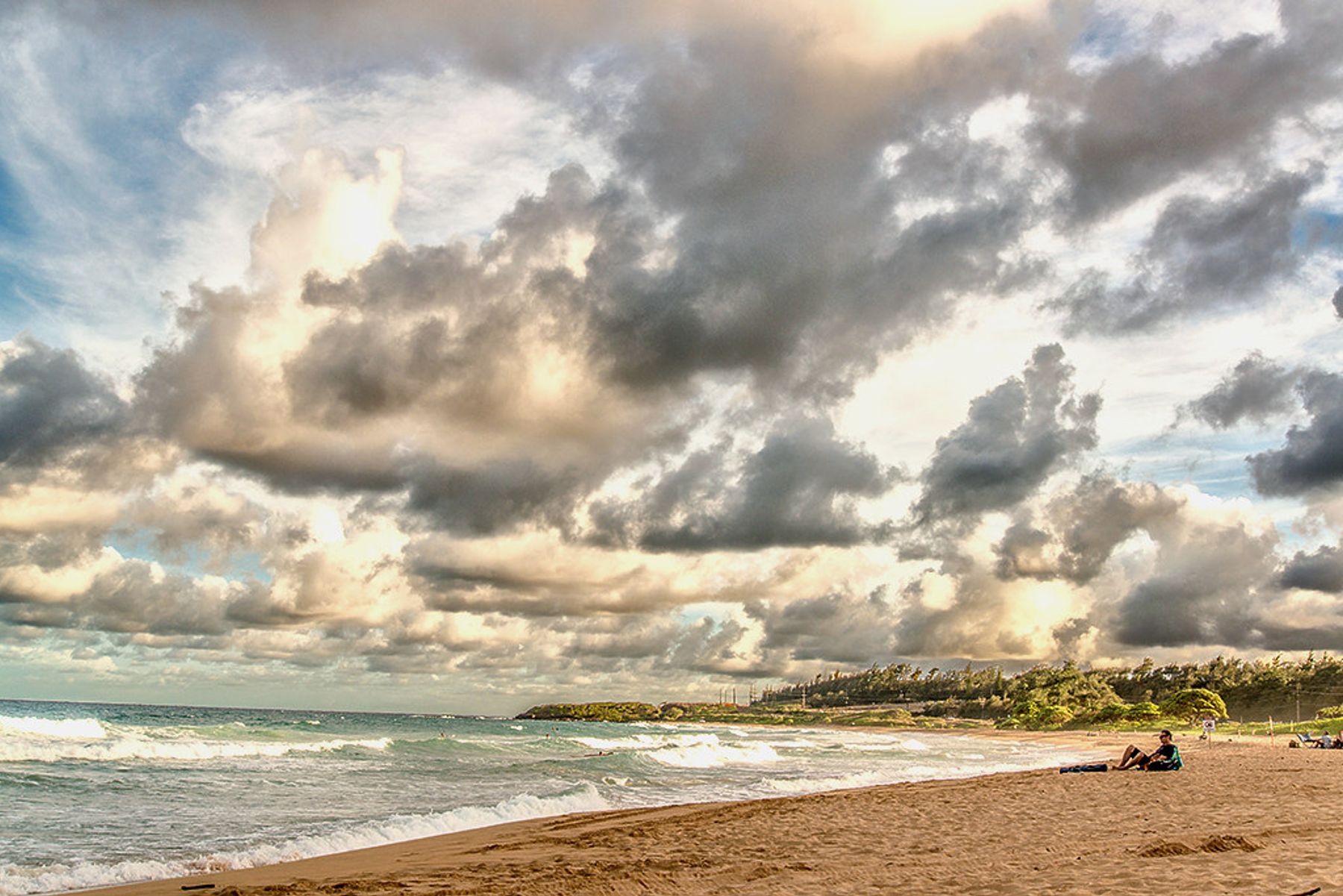 Dusk clouds over Keālia Beach with rolling waves, wide sand, and a curving shoreline toward a distant headland