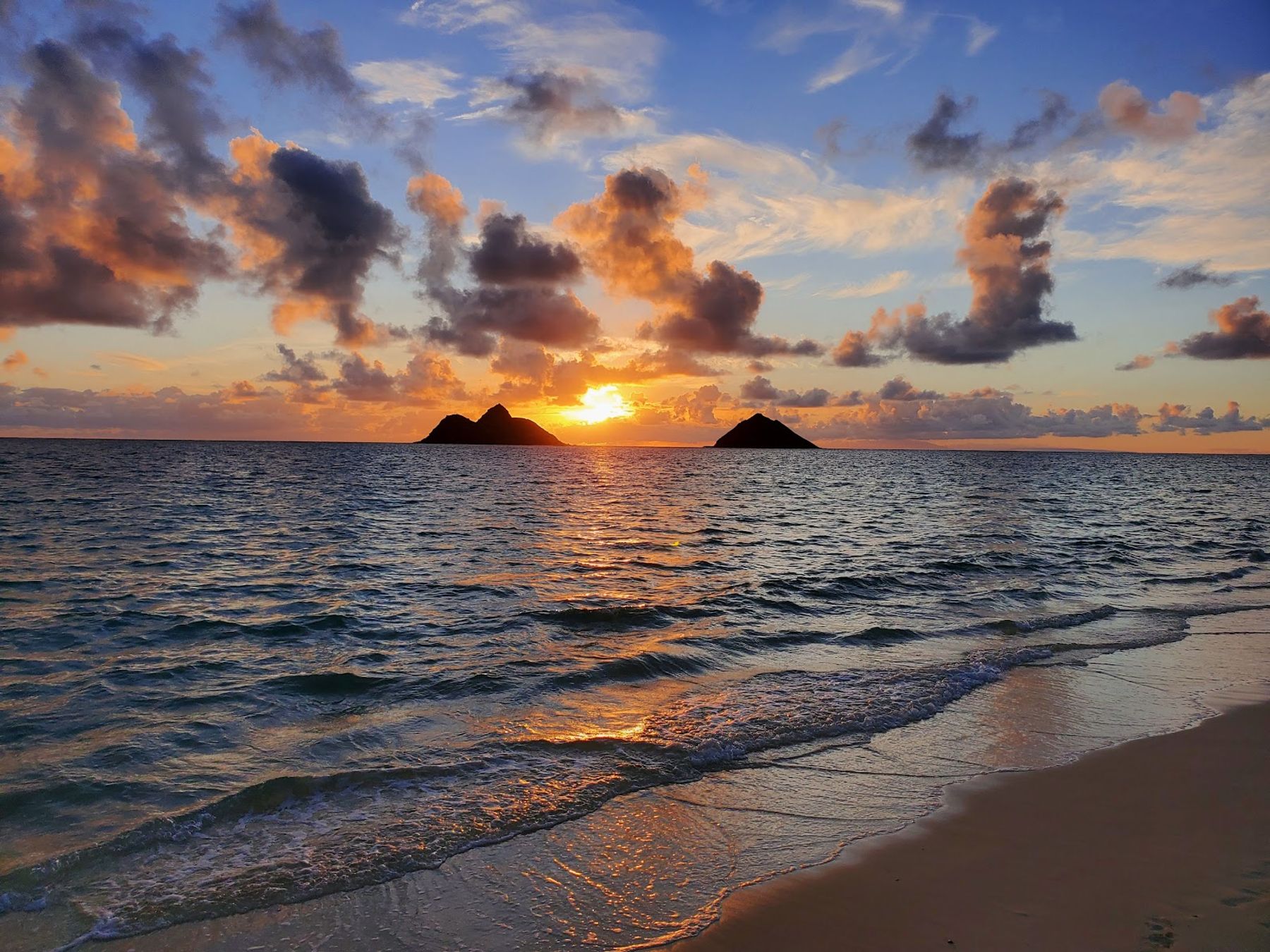 Sunrise over the Mokulua Islands from the waterline at Lanikai Beach.