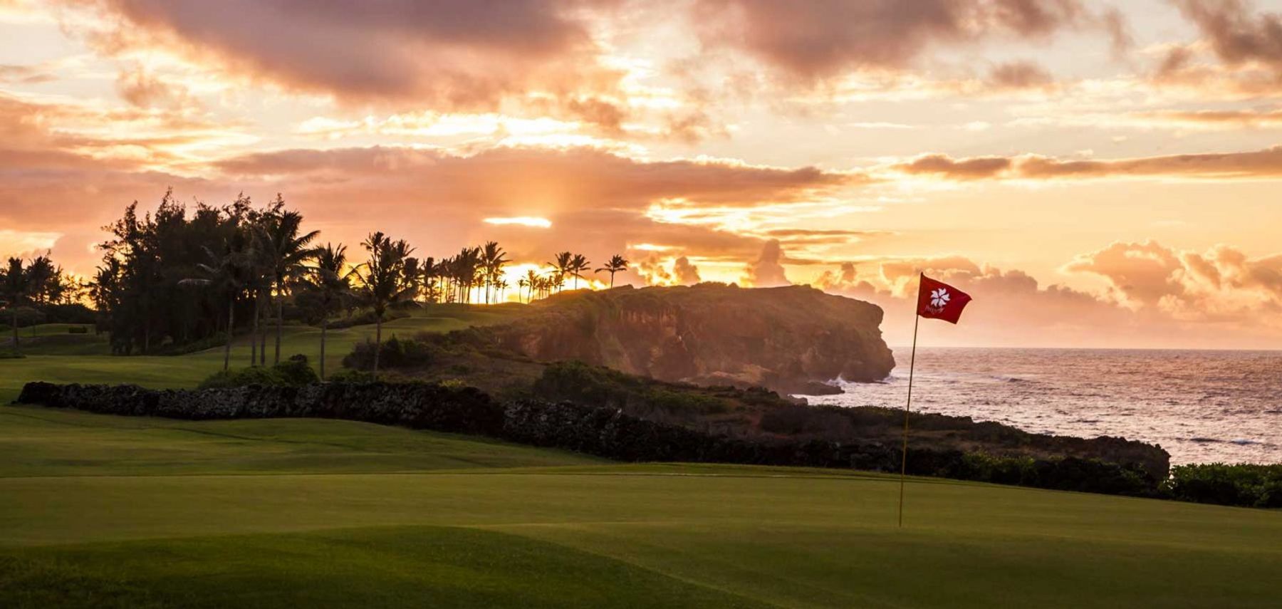 Stunning oceanfront golf green at Poipu Bay Golf Course during sunset with dramatic cliffs and palm trees