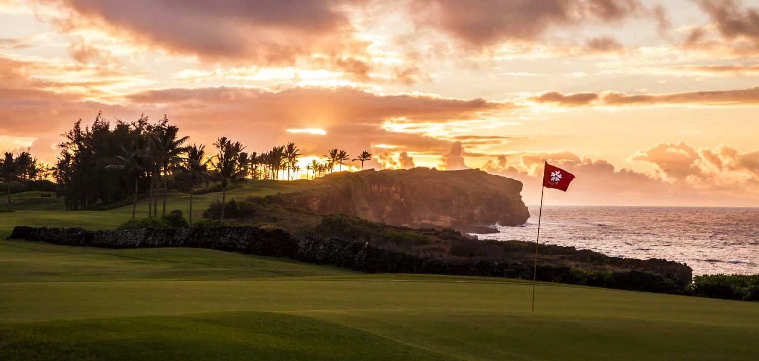 Stunning oceanfront golf green at Poipu Bay Golf Course during sunset with dramatic cliffs and palm trees