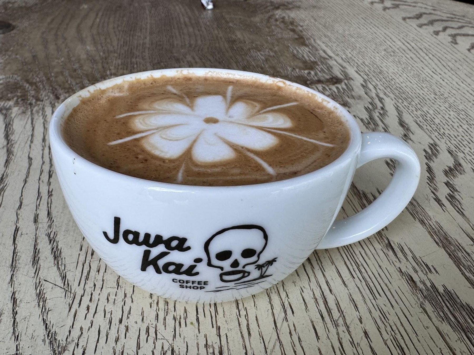 Artfully crafted latte with hibiscus flower foam art in a Java Kai branded cup