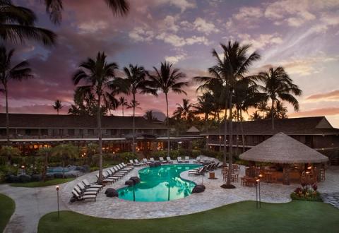 Romantic sunset view of Ko a Kea Resort pool with tiki bar and palm trees silhouettes