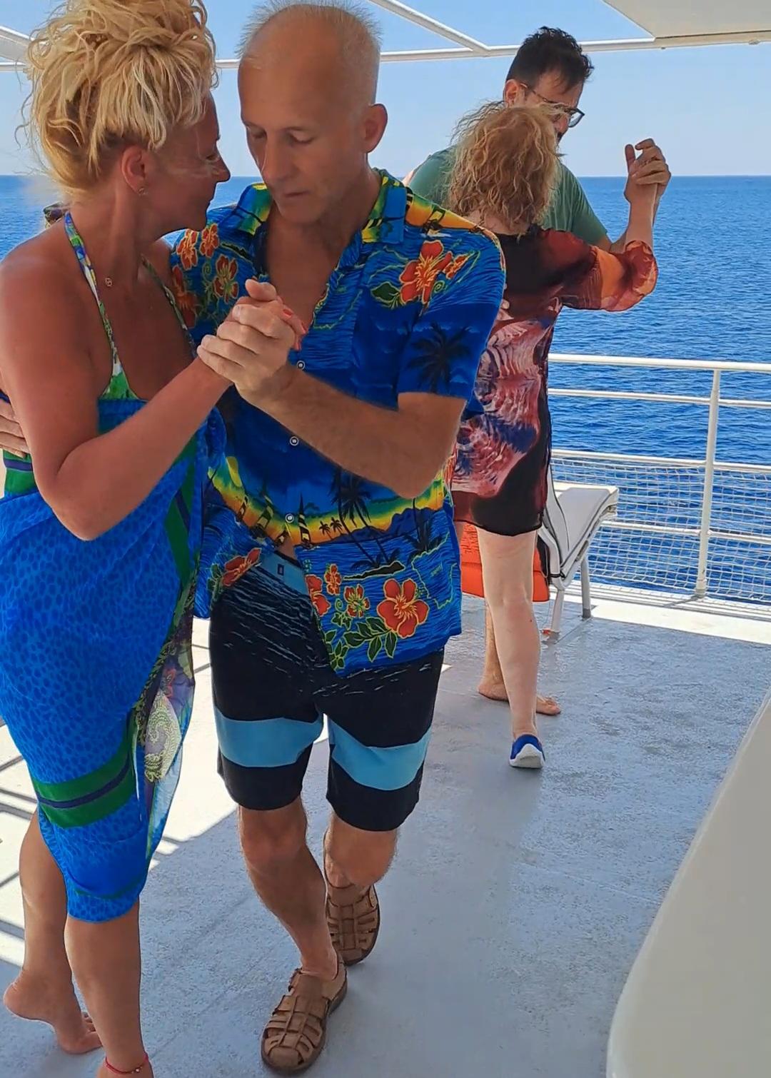 Two couples dancing tango on the boat deck with the sea behind them.