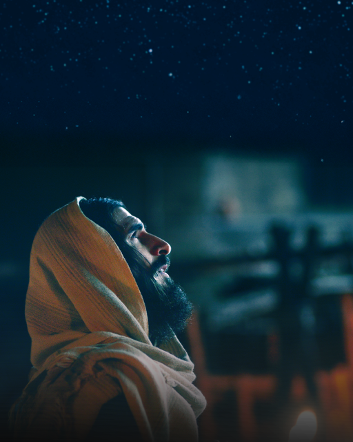 Jesus, his head covered, looks up at a night sky full of stars
