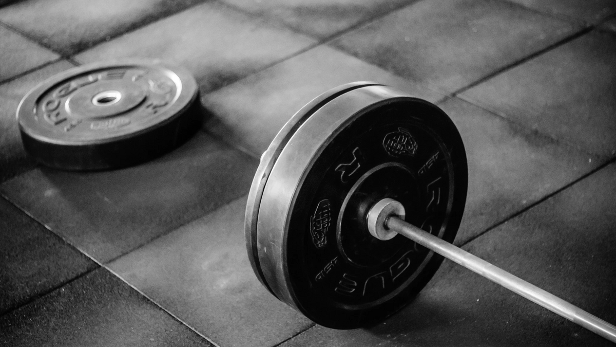 A black and white image of a barbell sits on a stone floor.