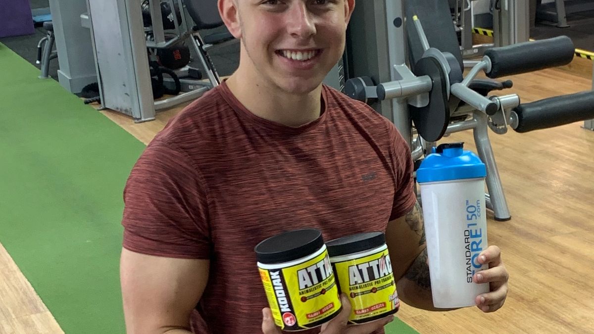 Alex Standing In The Gym Holding Supplements