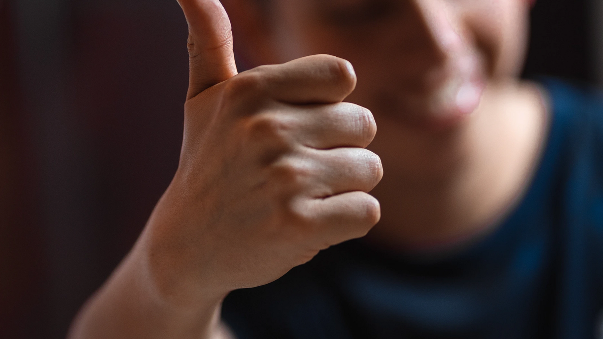 Man putting his thumb up at the camera. The thumb and hand are in focus while the mans face and body are out of focus