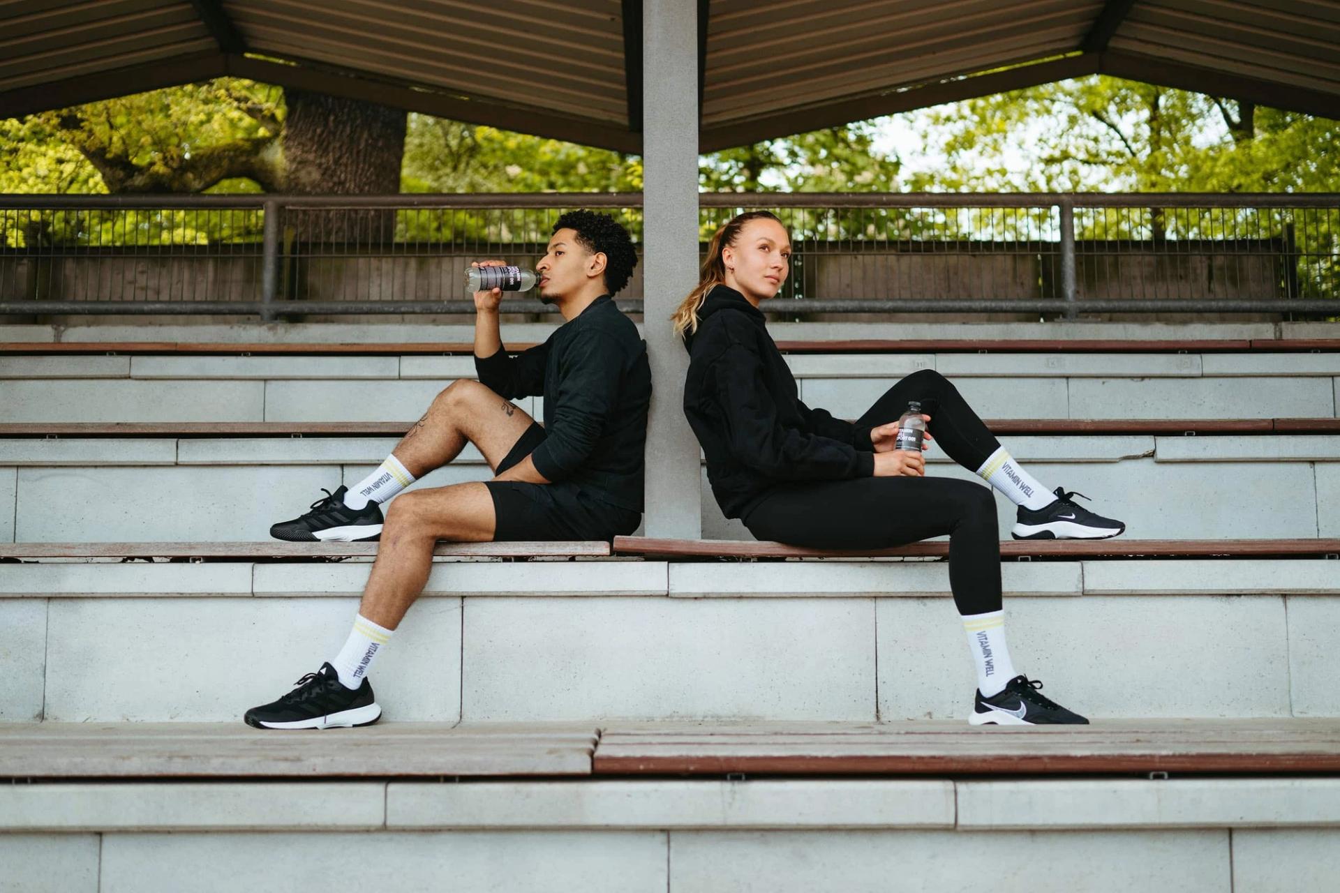 Two athletes sitting back-to-back under a pavilion with Vitamin Well bottles — Björn Lexius, Hamburg