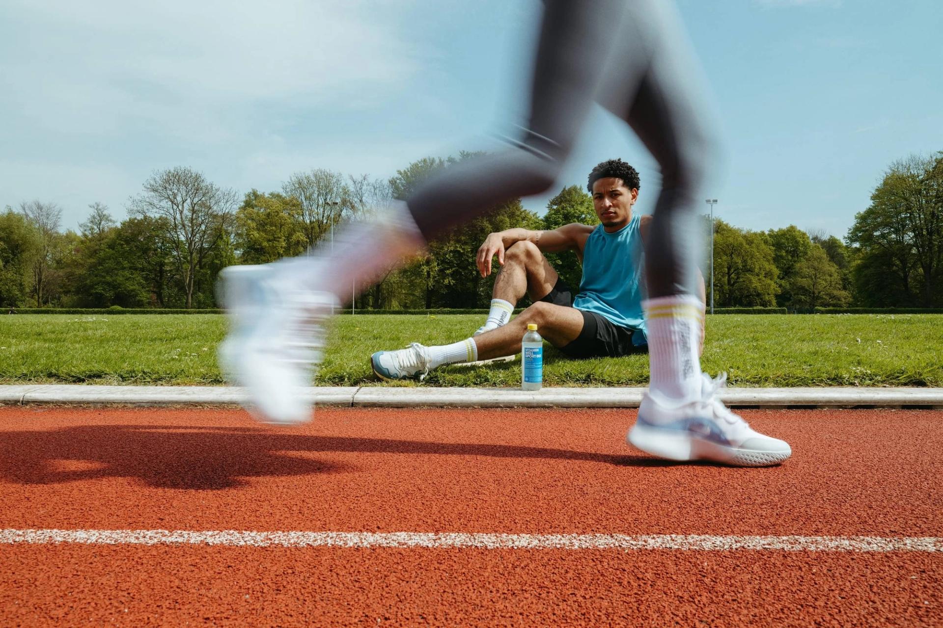 Blurred runner passing a seated athlete on the track — Björn Lexius, Hamburg