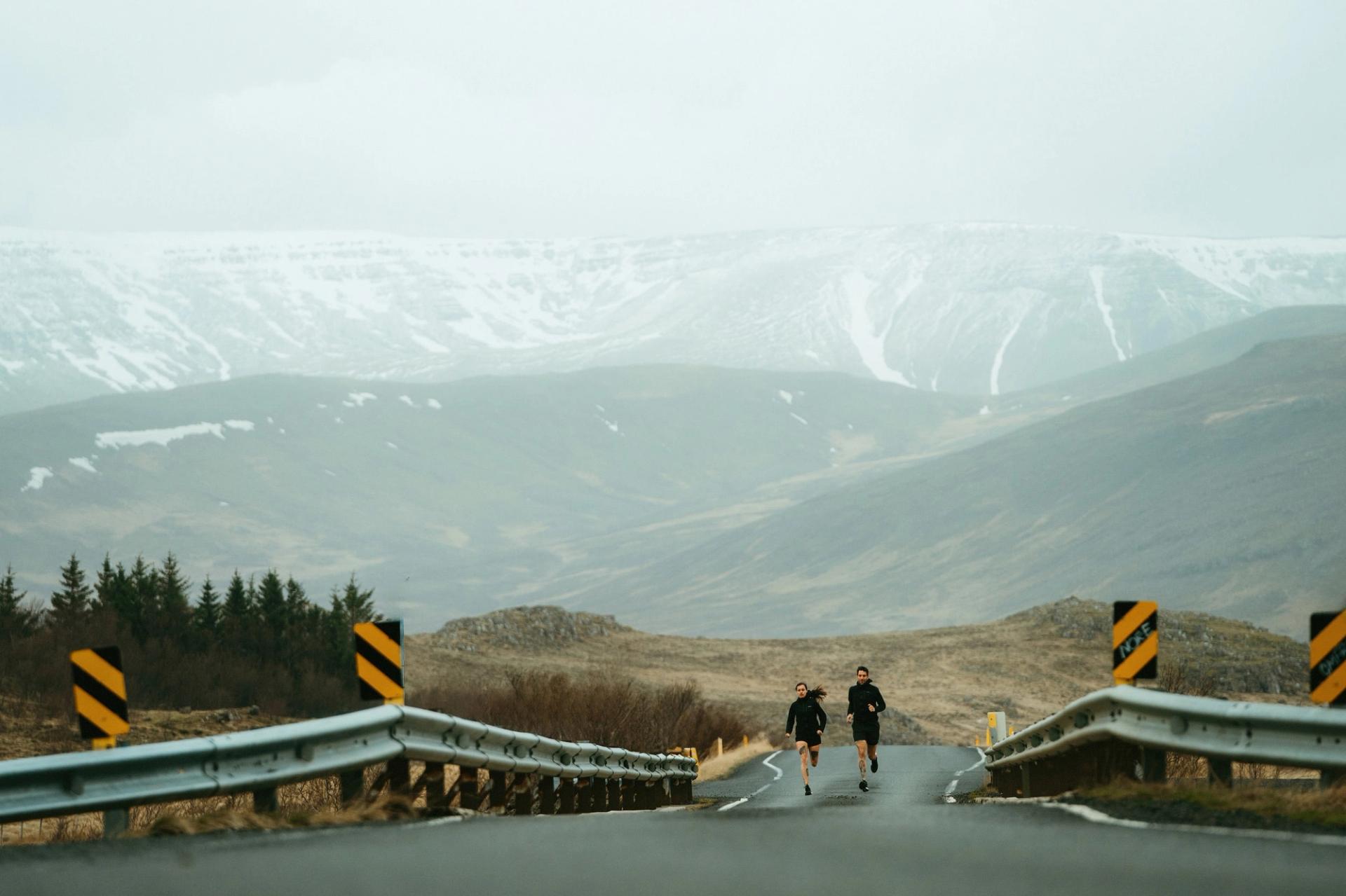 Two runners on a bridge with snow-capped mountains in the distance — Björn Lexius, Iceland