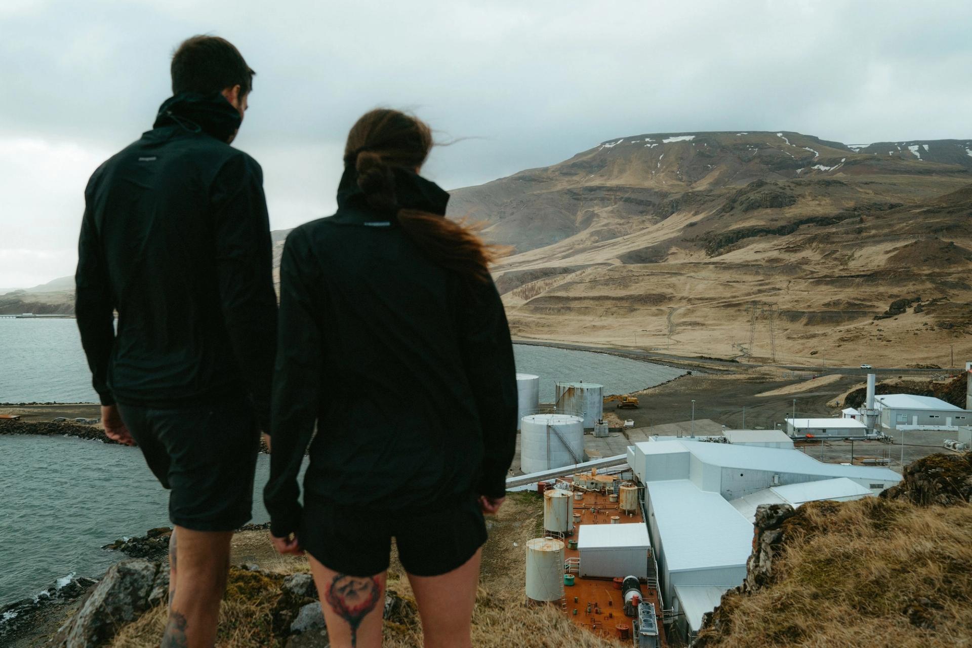 Two runners looking out over an industrial harbor from a cliff — Björn Lexius, Iceland