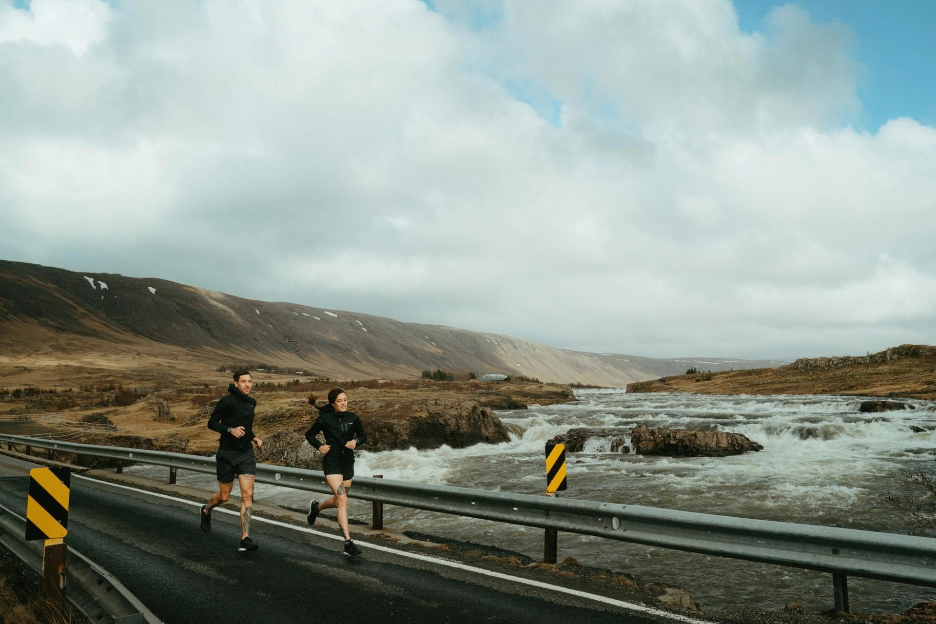 Two runners crossing a bridge above a rushing glacial river — Björn Lexius, Iceland