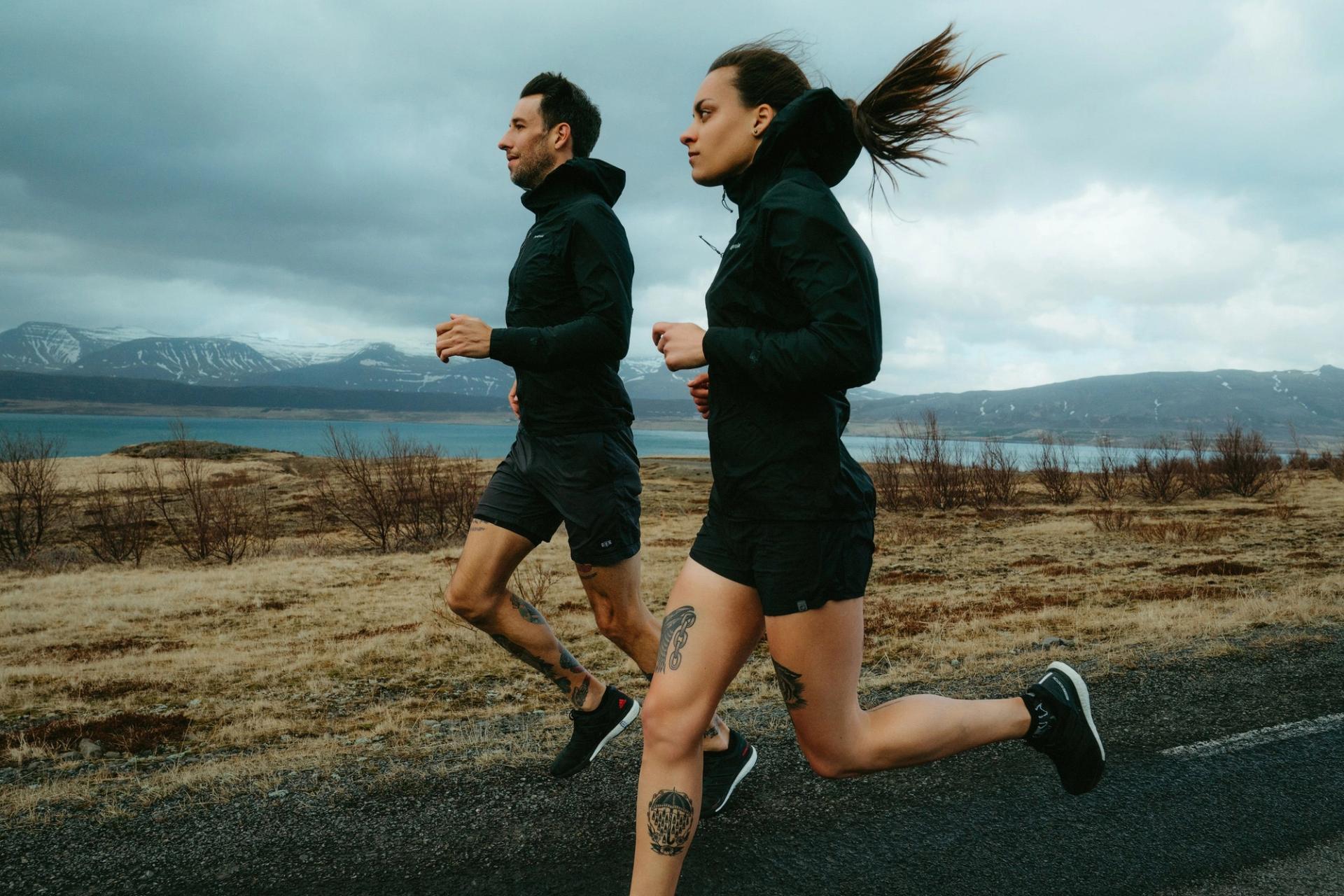 Two runners jogging along a road beside a lake, hair blowing — Björn Lexius, Iceland
