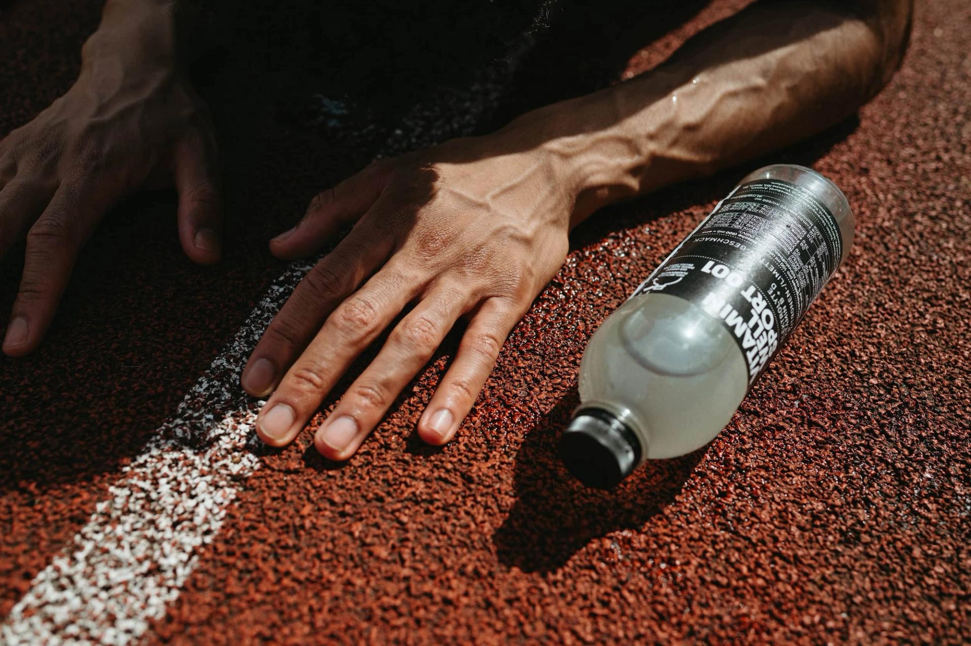 Close-up of forearm on running track next to Sport 001 bottle — Björn Lexius, Hamburg