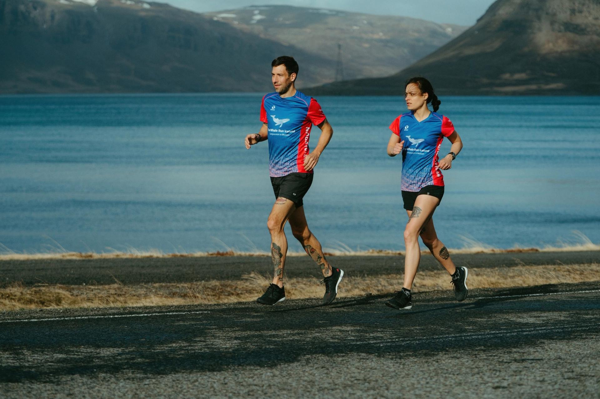 Two runners in The Whale Run Iceland jerseys beside a fjord — Björn Lexius, Iceland