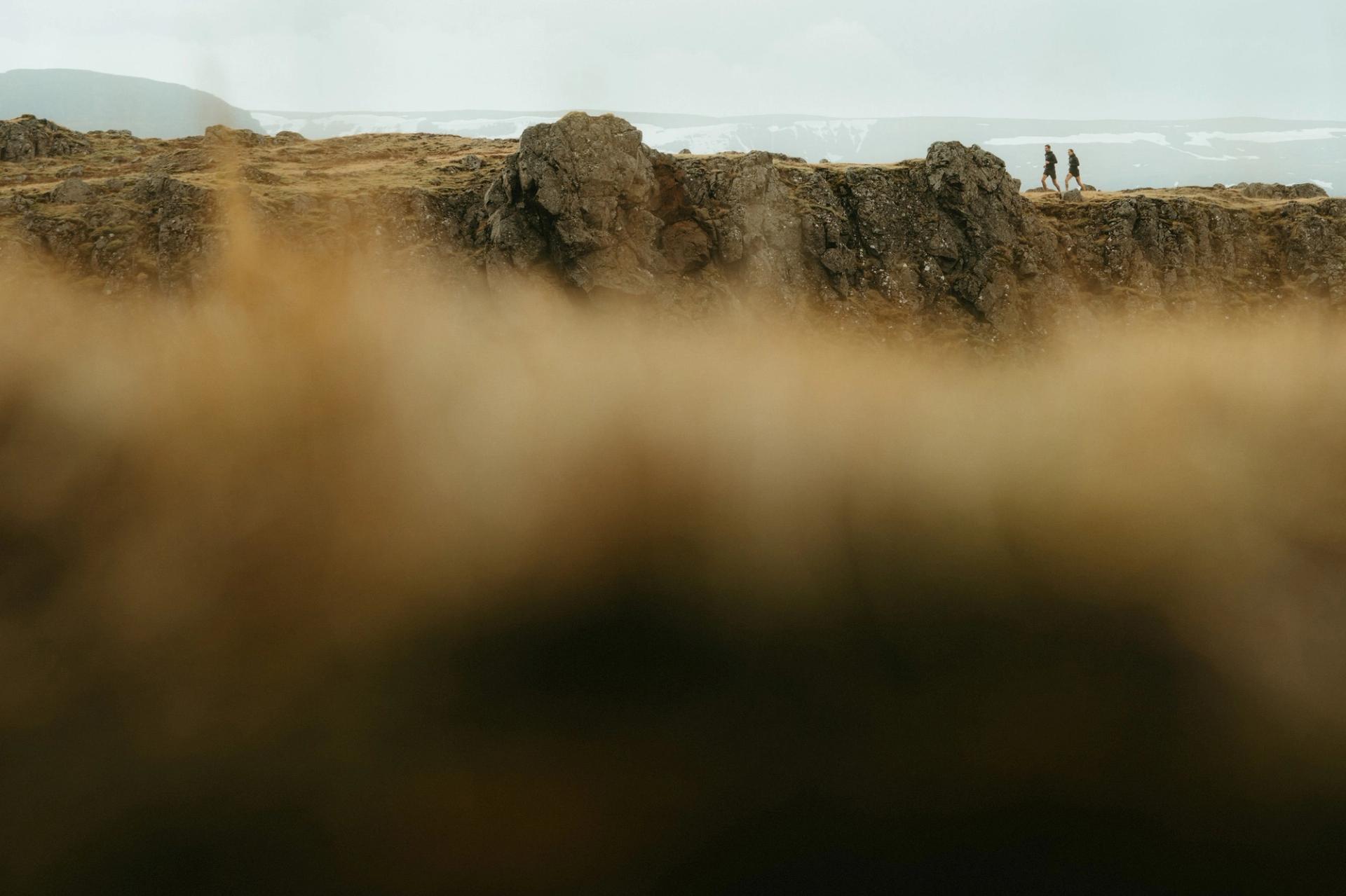 Two runners crossing a rocky ridge with snow-capped mountains behind — Björn Lexius, Iceland