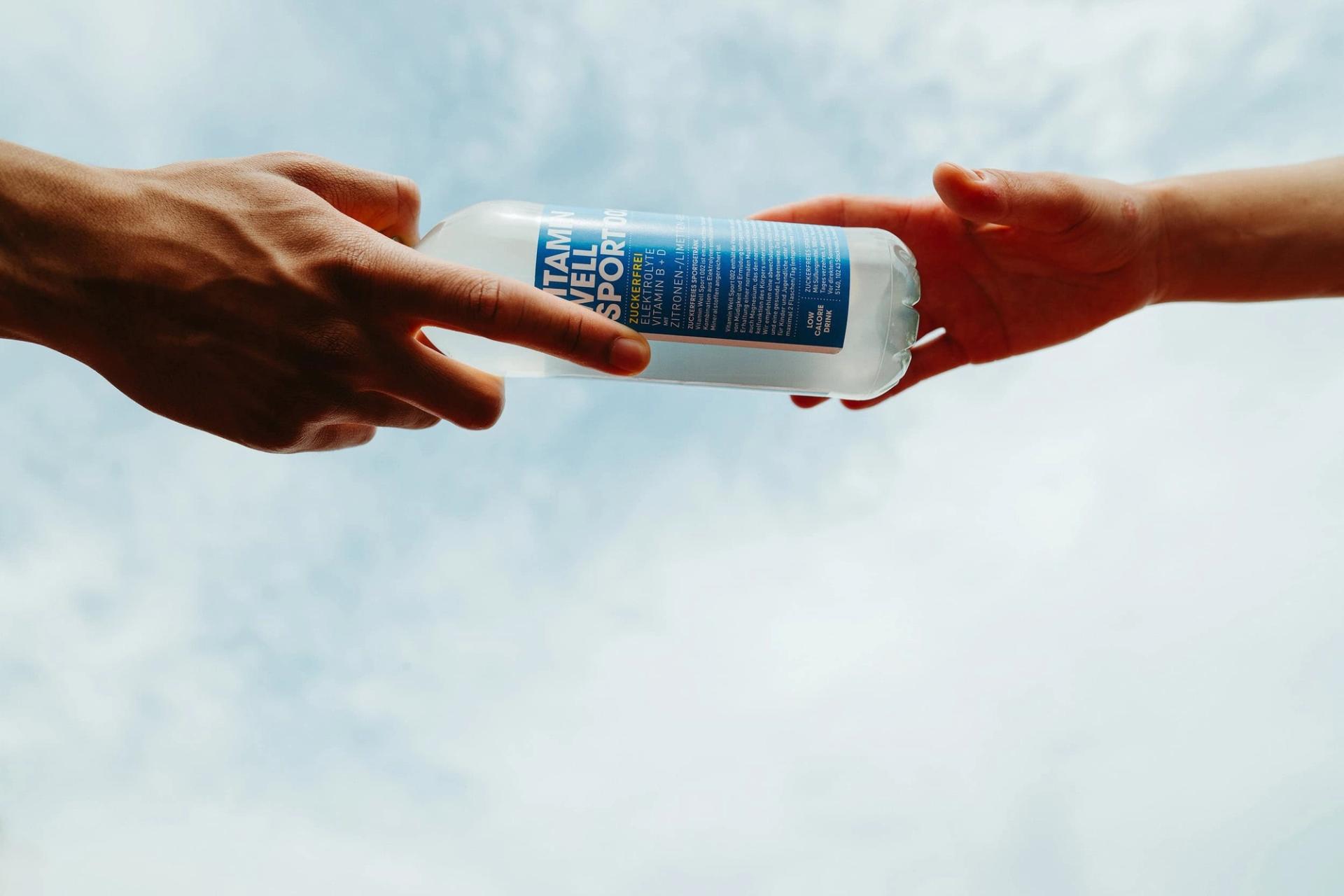 Two hands passing a Vitamin Well Sport 001 bottle against the sky — Björn Lexius, Hamburg