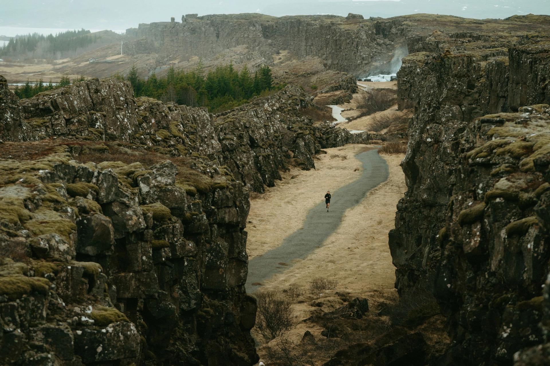 Solo runner on a sand path between volcanic rock walls — Björn Lexius, Iceland