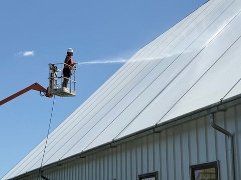 Premier Power Washing technician soft washing a commercial metal building roof from a boom lift
