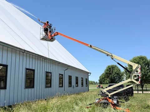 Premier Power Washing crew soft washing a large commercial metal building roof with a boom lift