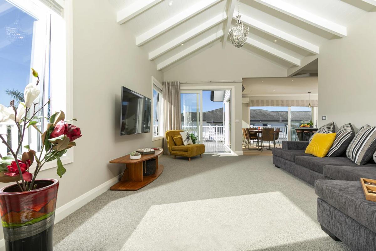 Living room with a raked ceiling and exposed white beams, opening to the deck
