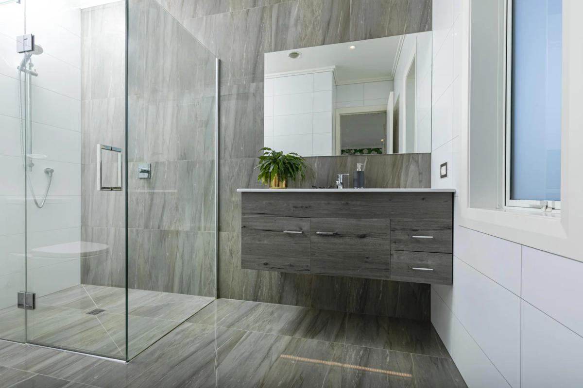 Bathroom with large format grey tiles, a glass shower and floating timber vanity
