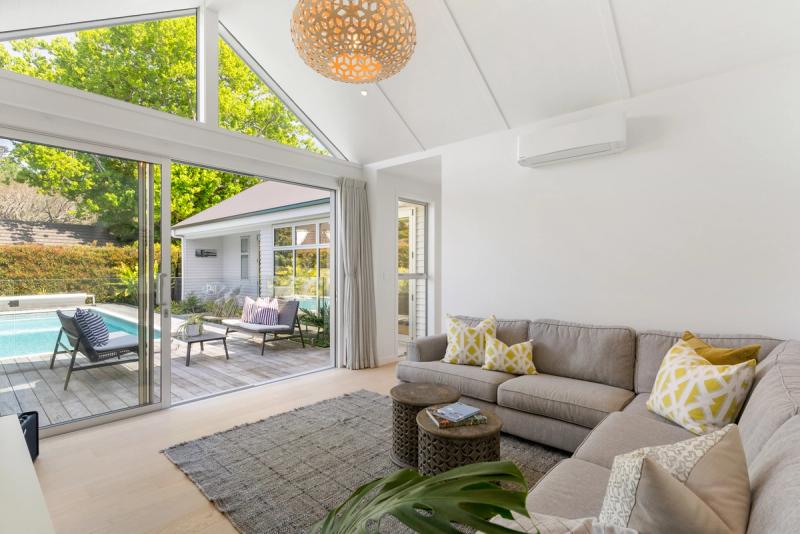 Open plan living room with a raked ceiling and woven pendant light, opening to the pool deck