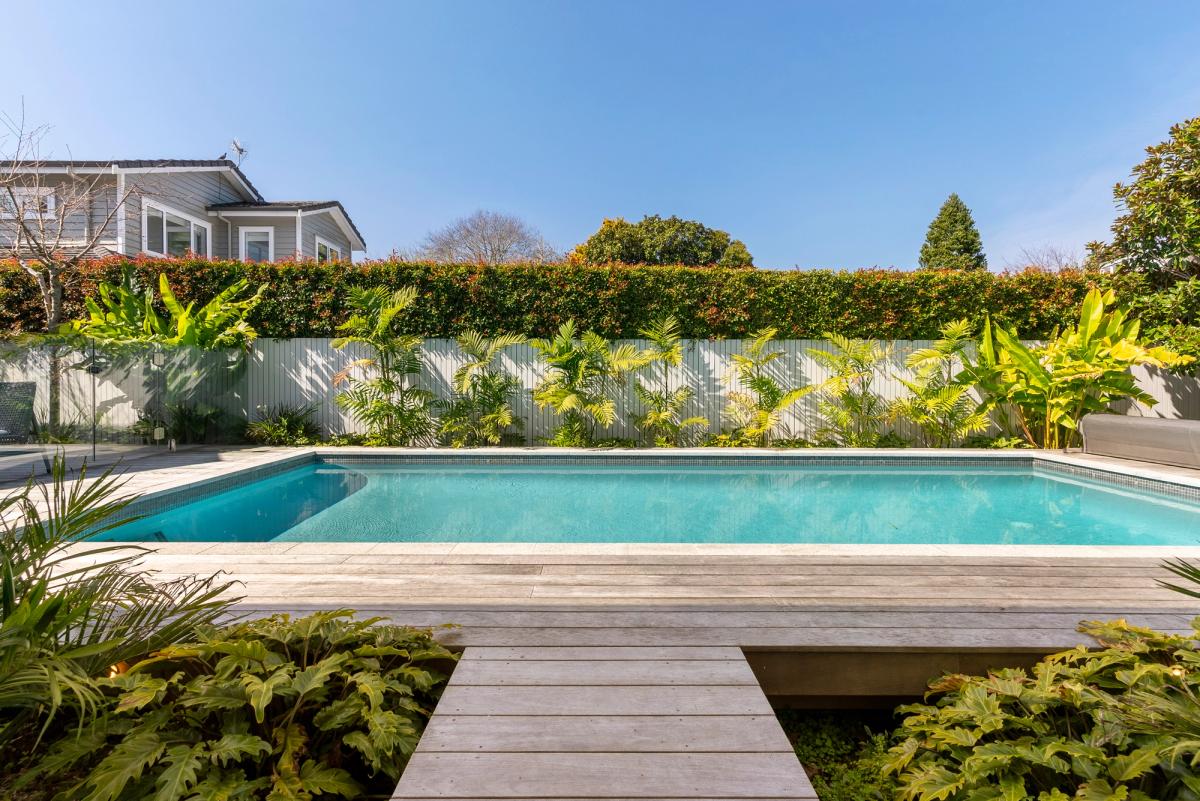 Swimming pool edged with timber decking and a planted boundary wall