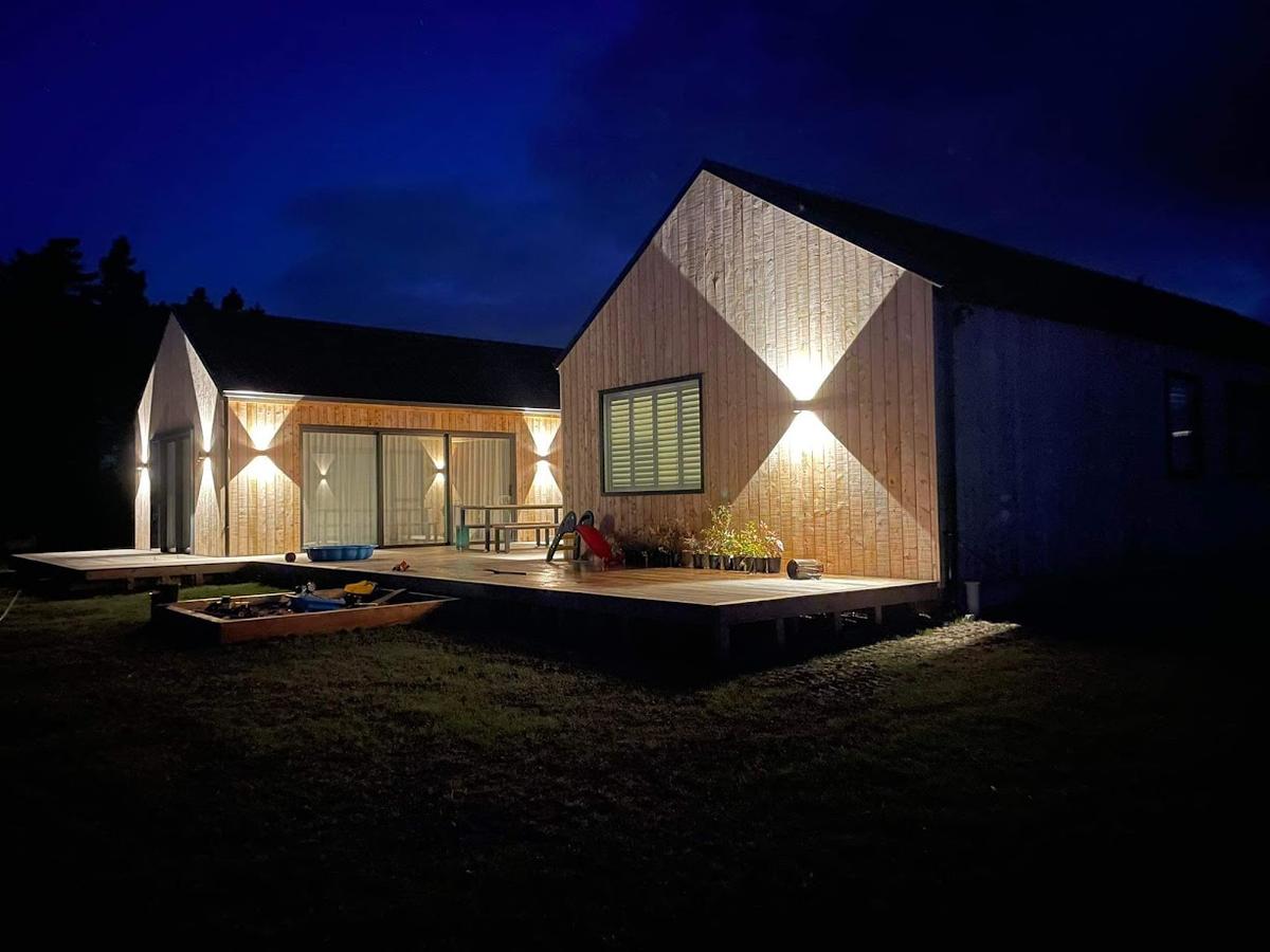 The pavilion lit at dusk, in timber and dark cladding