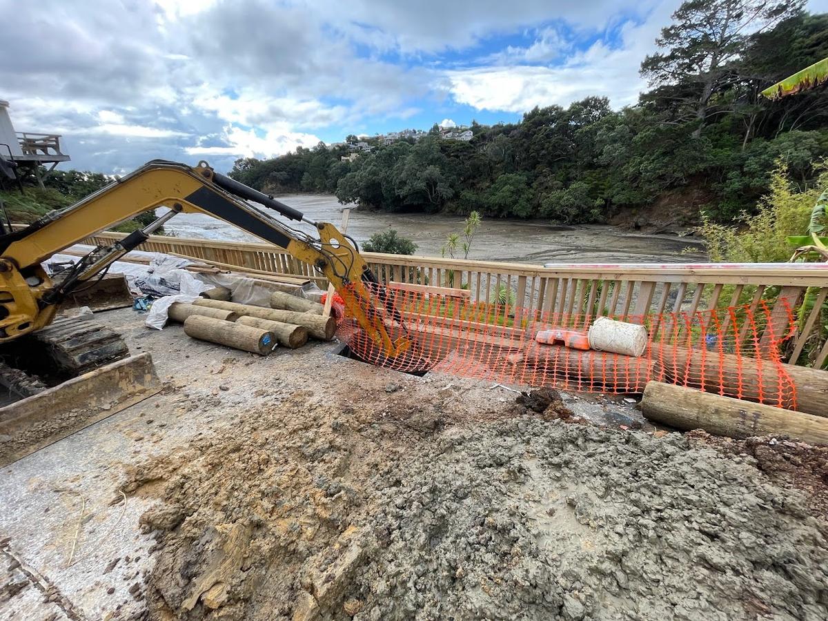 Excavator working alongside timber poles for the new retaining wall