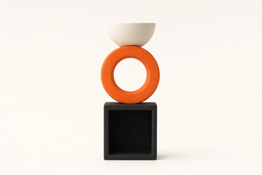 A vertical totem of three hollow matte ceramic forms stacked dead-on against a bone cream backdrop: a low open black cube at the bottom showing a square dark interior, a tangerine ring in the middle with its circular opening facing the camera, and a small ivory half-bowl at the top opening upward.