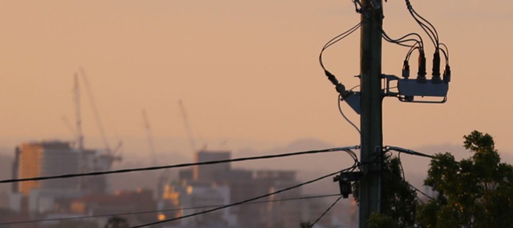 A shadowed NOJA Power OSM Recloser Installation with city infrastructure in the background, with an orange sunset in the background