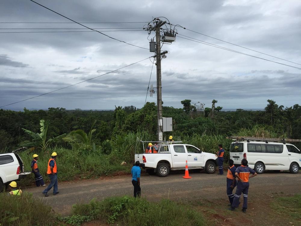 Group of men standing beside their cars looking at NOJA Power OSM Recloser Installation outside Suva on Viti Levu, Fiji.