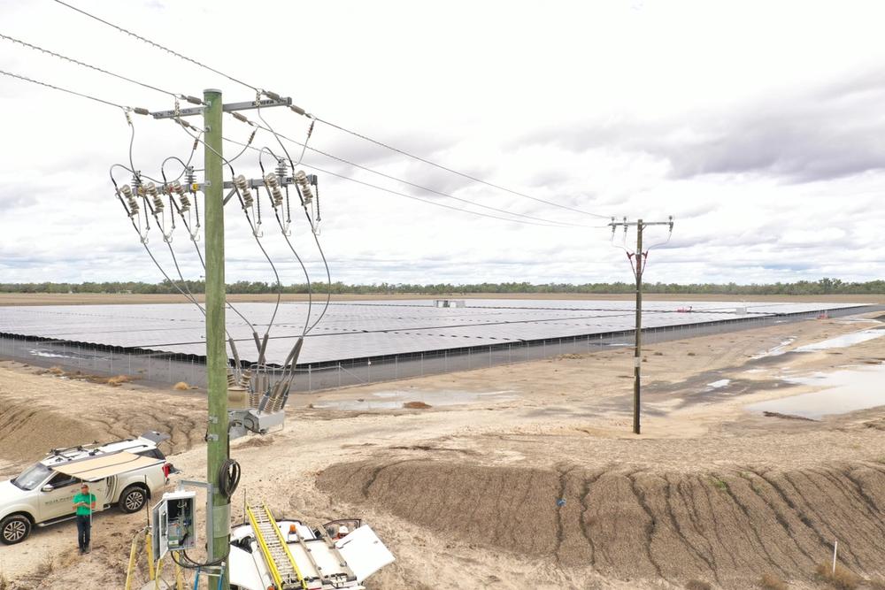 NOJA Power OSM Recloser with RC20 Control to the left front of image, with brown dirt below and solar farm in the background of the image