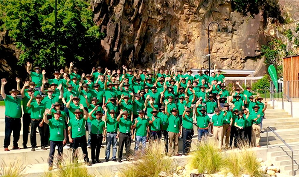 Group of NOJA Power partners standing in a group wearing green shirts and akubra hats waving to the camera 